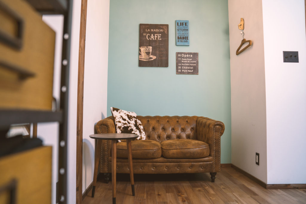 ウッドのフローリングにヴィンテージ感のあるブラウンの革製のソファがあり、淡いエメラルドグリーンの壁紙には木製の看板が飾られている店内の様子